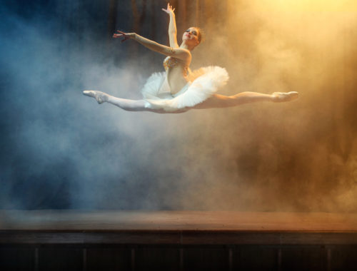 Ballet dancer performing on stage in theatre. There is a fog on the stage.