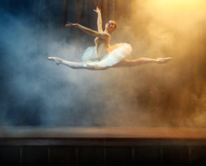 Ballet dancer performing on stage in theatre. There is a fog on the stage.